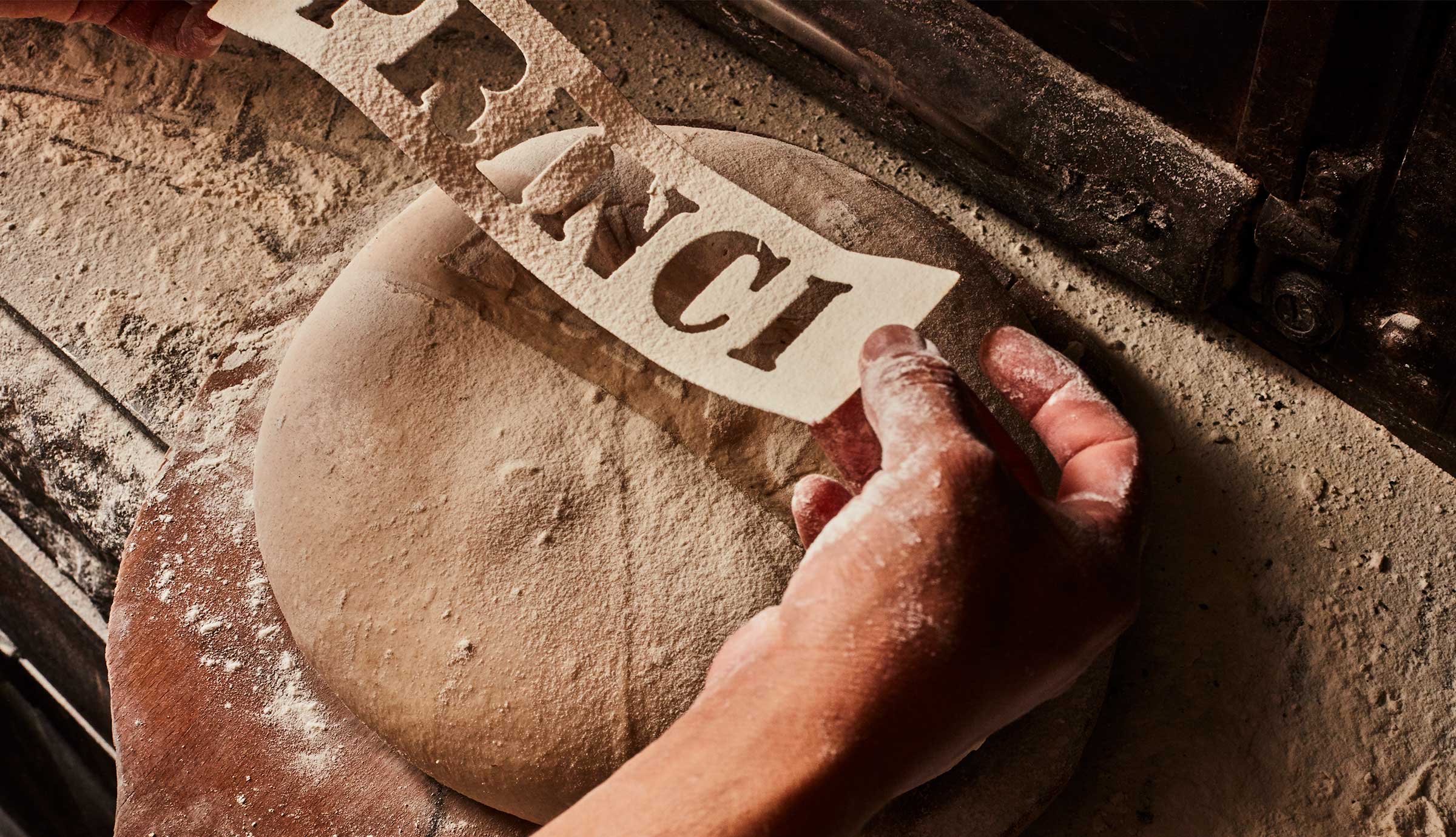 A stencil that reads Princi is held over bread dough